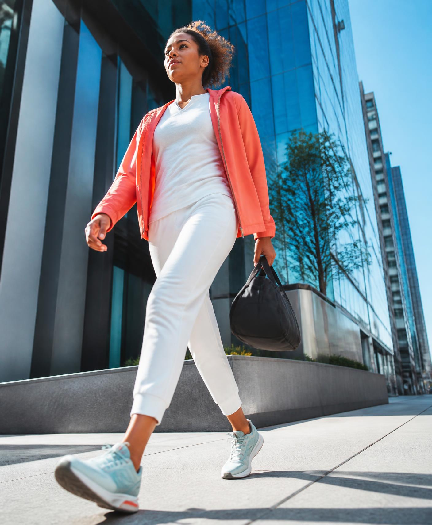 A young professional walking with purpose along a sunlit downtown sidewalk